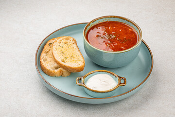 Portion of slavic traditional red sour soup borscht with toast and cream
