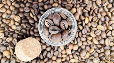 Coffee beans in a small glass jar with a cork lid on the table. Coffee beans packed in a transparent, airtight storage container. Coffee seeds inside a glass jar. Flat layout.