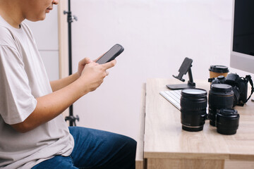 Photo editor or photographer using smartphone for uploading to social media at office desk.