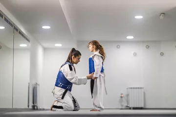 Tuinposter Taekwondo kid is standing at martial art school and her teammate is adjusting her dobok. © dusanpetkovic1