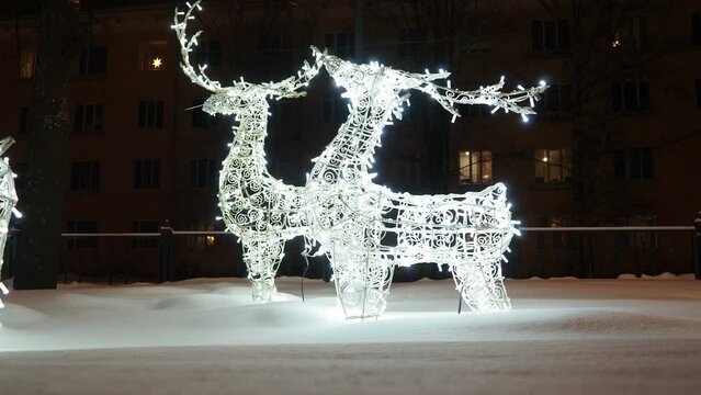 Glowing deer. Festive New Year Christmas electrical art installation, architecture structure in snowdrift. Light decoration of city street. Winter night. Garlands of light bulbs shine in silver. Xmas