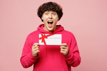 Young shocked surprised Caucasian man wears hoody casual clothes hold gift certificate coupon voucher card for store isolated on plain pastel light pink background studio portrait. Lifestyle concept.