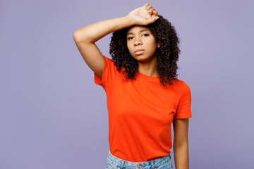 Little tired ill sick kid teen girl of African American ethnicity wear orange t-shirt put hand on forehead suffer from headache isolated on plain pastel purple background. Childhood lifestyle concept - obrazy, fototapety, plakaty