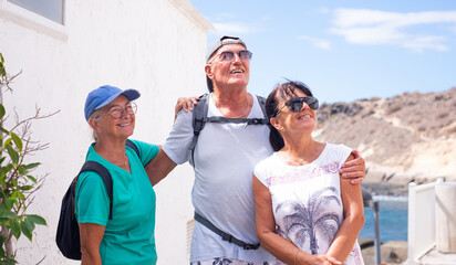 Cheerful group of caucasian senior friends outdoors looking at seascape. Elderly people walking...