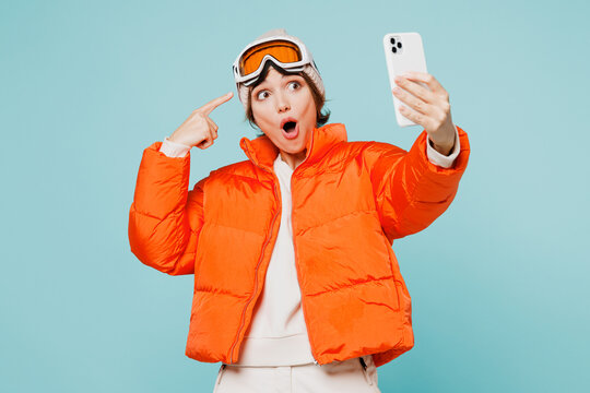 Skier young woman wearing padded windbreaker jacket hat ski point goggles mask do selfie shot mobile cell phone travel rest spend weekend winter season in mountains isolated on plain blue background.