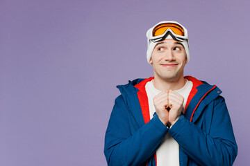 Skier man wear warm blue windbreaker jacket ski goggles mask hold fists folded together look aside on area spend weekend winter season in mountains isolated on plain purple background. Hobby concept.