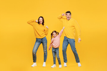 Fototapeta premium Full body young fun happy parents mom dad with child kid girl 7-8 years old wear pink sweater casual clothes do winner gesture dance show v-sign isolated on plain yellow background Family day concept