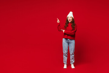 Full body amazed young woman she wears knitted sweater white hat casual clothes point index finger aside on area look camera isolated on plain red color background studio portrait. Lifestyle concept. © ViDi Studio