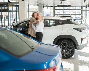 Mature Caucasian couple hugging with happiness while buying a new car. 