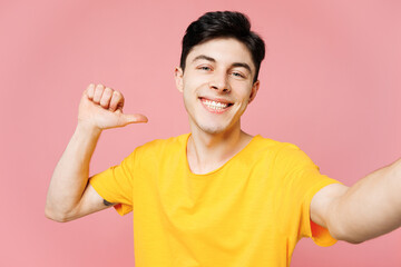 Young smiling man he wears yellow t-shirt casual clothes doing selfie shot pov on mobile cell phone point finger on himaself isolated on plain pastel light pink background studio. Lifestyle concept.