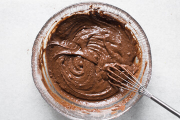 chocolate cake batter in a glass mixing bowl, process of making chocolate muffins or chocolate cake