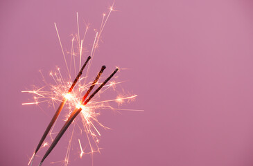 Fototapeta premium Burning sparklers burning on pink background, copy space for text.