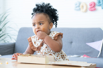 Portrait of Cute African child eating pizza at home party. Kid enjoy and having fun with tasty...