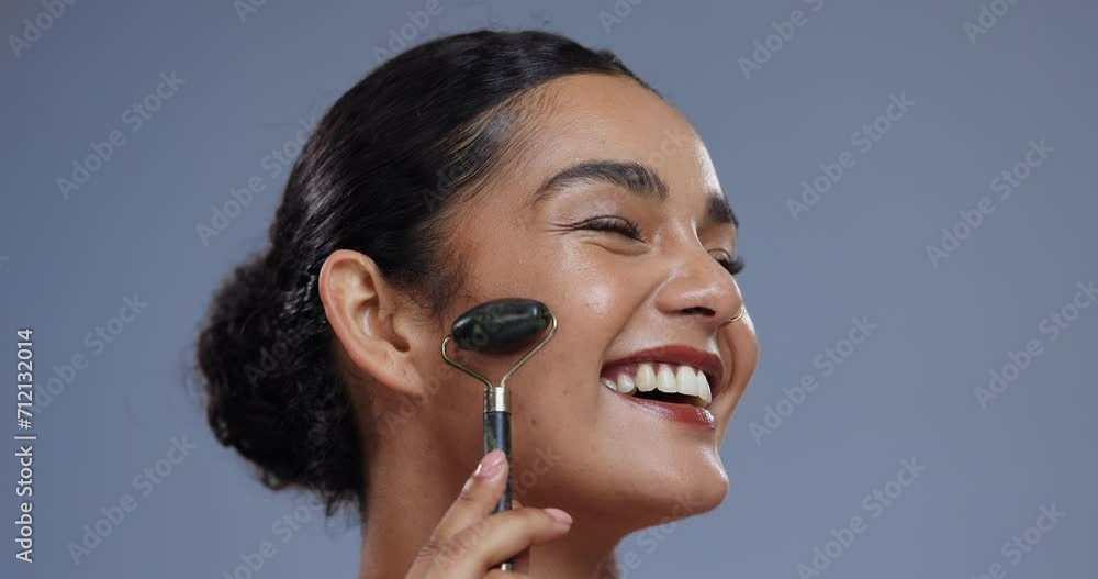 Wall mural Beauty, skincare and happy woman with face roller, cosmetics and healthy skin glow in studio. Smile, dermatology and natural jade stone massage, girl on blue background with care, shine and facial.