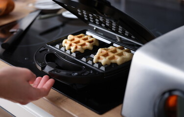 Waffle pastry baking on waffle maker machine closeup. Making waffles at home concept