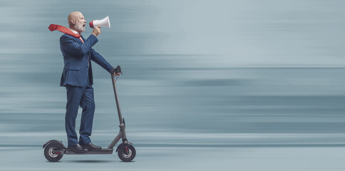 Businessman riding an e-scooter and shouting through a megaphone