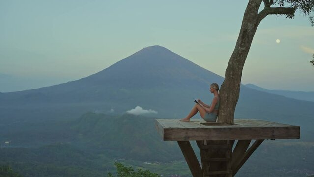 Woman writing emotions in journal at tropical viewpoint, Mental Health concept