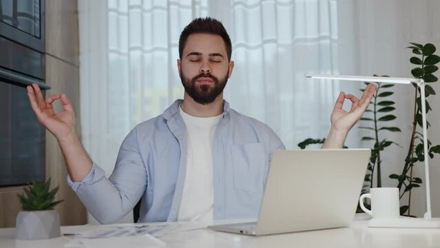 Irritated employee taking break from work for meditating with gyan mudra and closed eyes while breathing deep. Caucasian support manager ending correspondence with difficult client and calming down.