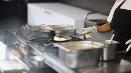 Close-up of cook prepares omelet in skillet in kitchen, cooking in cafes and restaurants. Professional chef making dessert, lunch for sale. Food concept