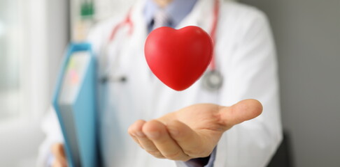 Close-up of cardiologist throw red plastic heart and catch it in palm, save life through donation...