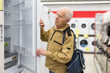 Elderly man choosing refrigerator in showroom of electrical appliance store