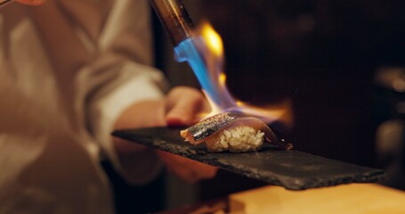 Hand, sushi and fire with chef in kitchen of restaurant for luxury or traditional cuisine closeup....