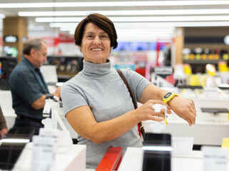 Older woman picking out new smartwatch to buy in electronics department of supermarket