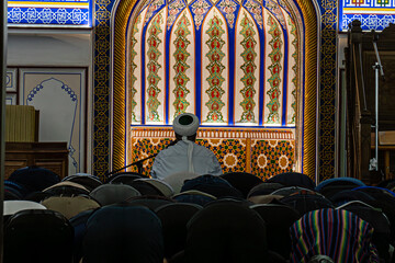 People in a Mosque. Muslims kneeling and bowing down while offering prayers during the Muslim festival of Eid. imam reads a prayer - obrazy, fototapety, plakaty