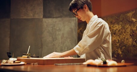Chef, restaurant or japanese sushi as fish, raw salmon or healthy food for local culture in kitchen. Asian man, hands and skill in rice on wood board, table and catering of seafood menu for nutrition