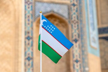 Waving Flag of Uzbekistan against the background of the madrasah. Uzbekistan a small souvenir flag symbol of state on wavy cotton fabric. - obrazy, fototapety, plakaty