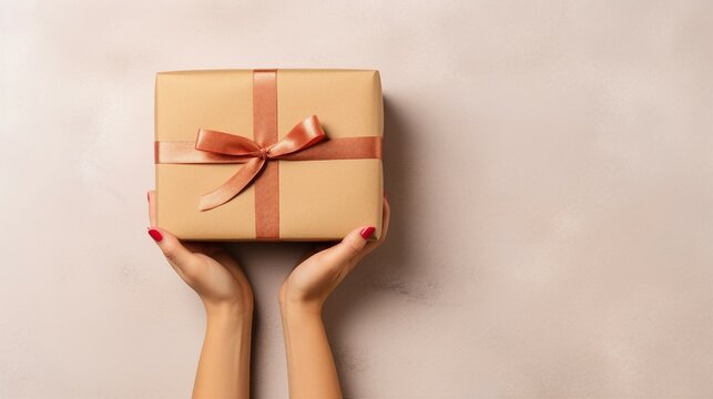 Experienced microstock contributor captures the essence of a young woman's hands, holding a kraft paper giftbox in a top view shot on an isolated beige background, optimizing for maximum visibility an