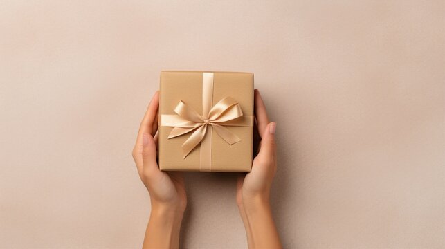 Experienced microstock contributor captures the essence of a young woman's hands, holding a kraft paper giftbox in a top view shot on an isolated beige background, optimizing for maximum visibility an