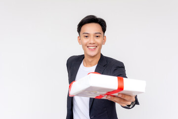 Joyful young asian man in a suit holding out a white gift with a red ribbon, exuding happiness and...