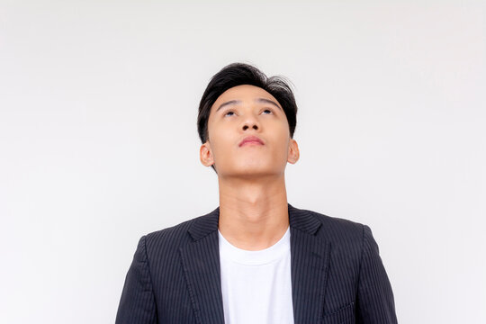 Young man in formal attire with a contemplative expression, looking upwards against a neutral background.