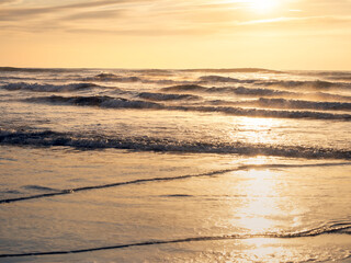 砂浜から見る朝陽に金色に輝く荒々しい海