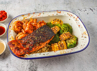Grilled salmon and shrimps with noodles, grilled corn and broccoli served in isolated on grey background top view of singaporean food