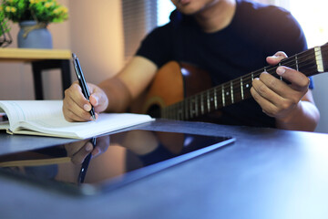 Man with acoustic guitar writing a note on the paper while music composition