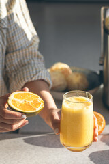 A glass of freshly squeezed orange juice and half an orange in female hands.