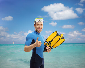 Man in a snorkeling suit holding swimming fins and showing thumbs up