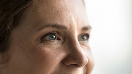 Blue eyes of young middle aged woman with black mascara on eyelashes looking away, smiling,...