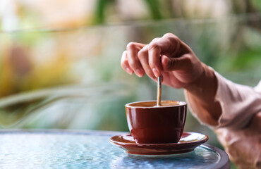 
Woman's hands holding a spoon and stirring hot coffee on the table