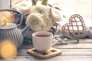 Cozy home composition with a cup of tea, teapot and flowers.