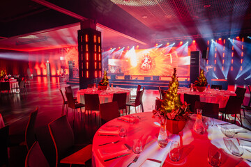  banquet hall with set tables, Christmas tree centerpieces, and a vibrant stage with red and blue...