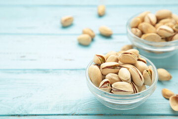 Bowl with pistachios on blue wooden background. Space for text