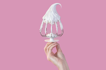 Woman's hand hold Whisk with cream, whisk with meringue cream isolated on pink photo - obrazy, fototapety, plakaty