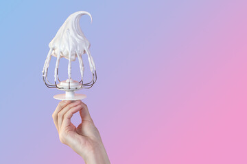 Woman's hand hold Whisk with cream, whisk with meringue cream isolated on gradient pink and blue...