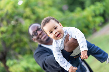 Father cuddling adorable biracial baby boy, little African American boy looking at camera bonding with dad outdoors - 712200472
