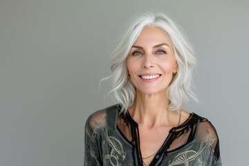Close-up portrait of half face of cheerful middle-aged Asian 50s woman with silver gray long hair, attractive lady looks at camera and laughing. Mature model with naked shoulders isolated on brown