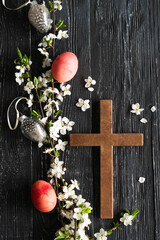 Spring cherry blossoms and Easter eggs and cross on old wooden background. Easter is a Christian...