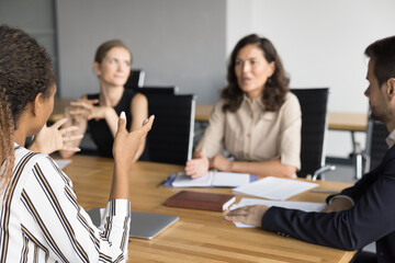 Cropped back view of young African American business woman sharing ideas with team of colleagues on office brainstorming meeting, discussing project management with elder colleague at table